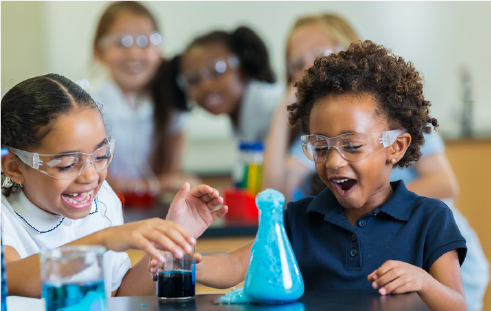 Schoolchildren with safety glasses laughing as they look at a beaker overflowing with blue bubbles (Students and Teachers impacted by COVID-19, Annual Letter, CZI).