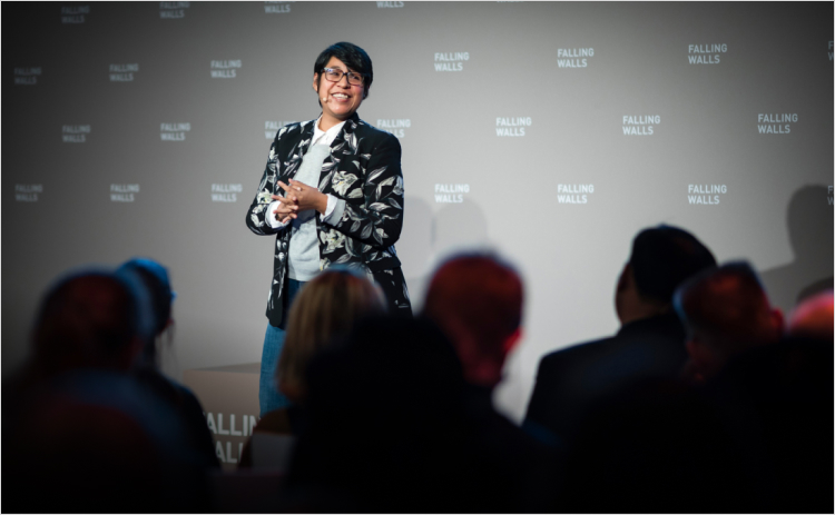 A presenter on stage talks to an audience at the 2019 Falling Walls Engage event.