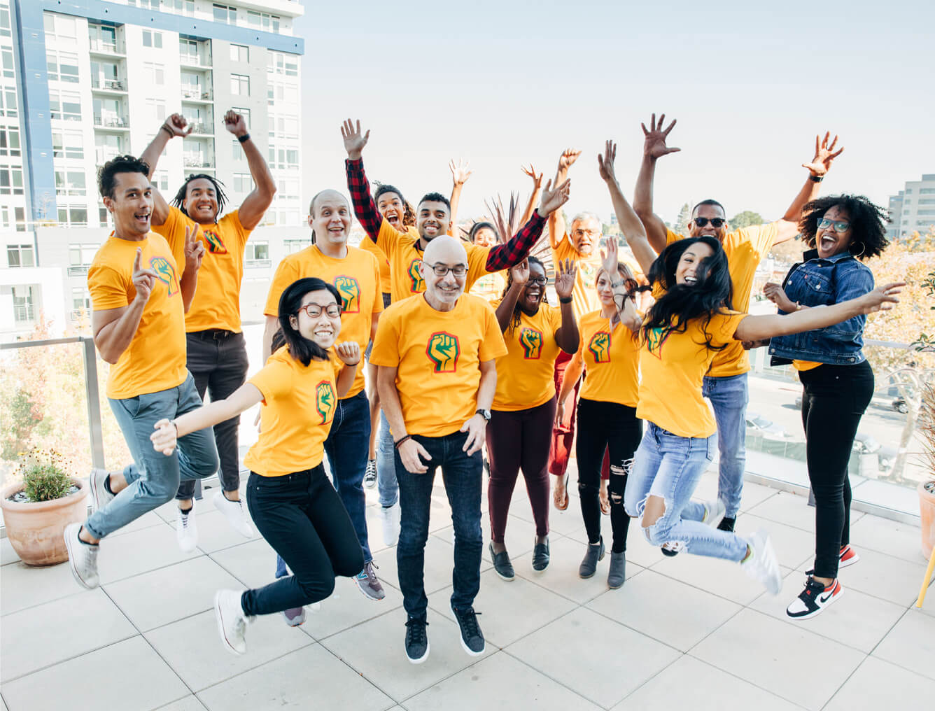 Group of CZI employees in symbolic power fist t-shirts, smiling and leaping in the air before heading out to AfroTech (Diversity, Equity, and Inclusion).