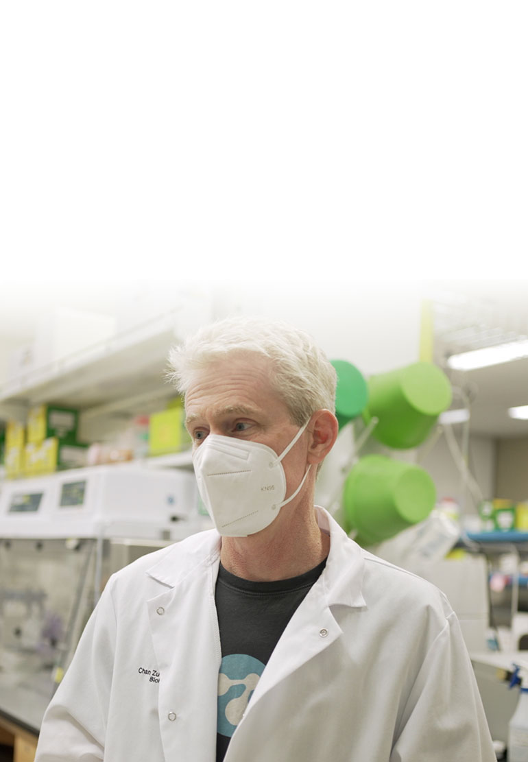 Joe DeRisi in white lab coat wears a N-95 mask in a COVID-19 lab.