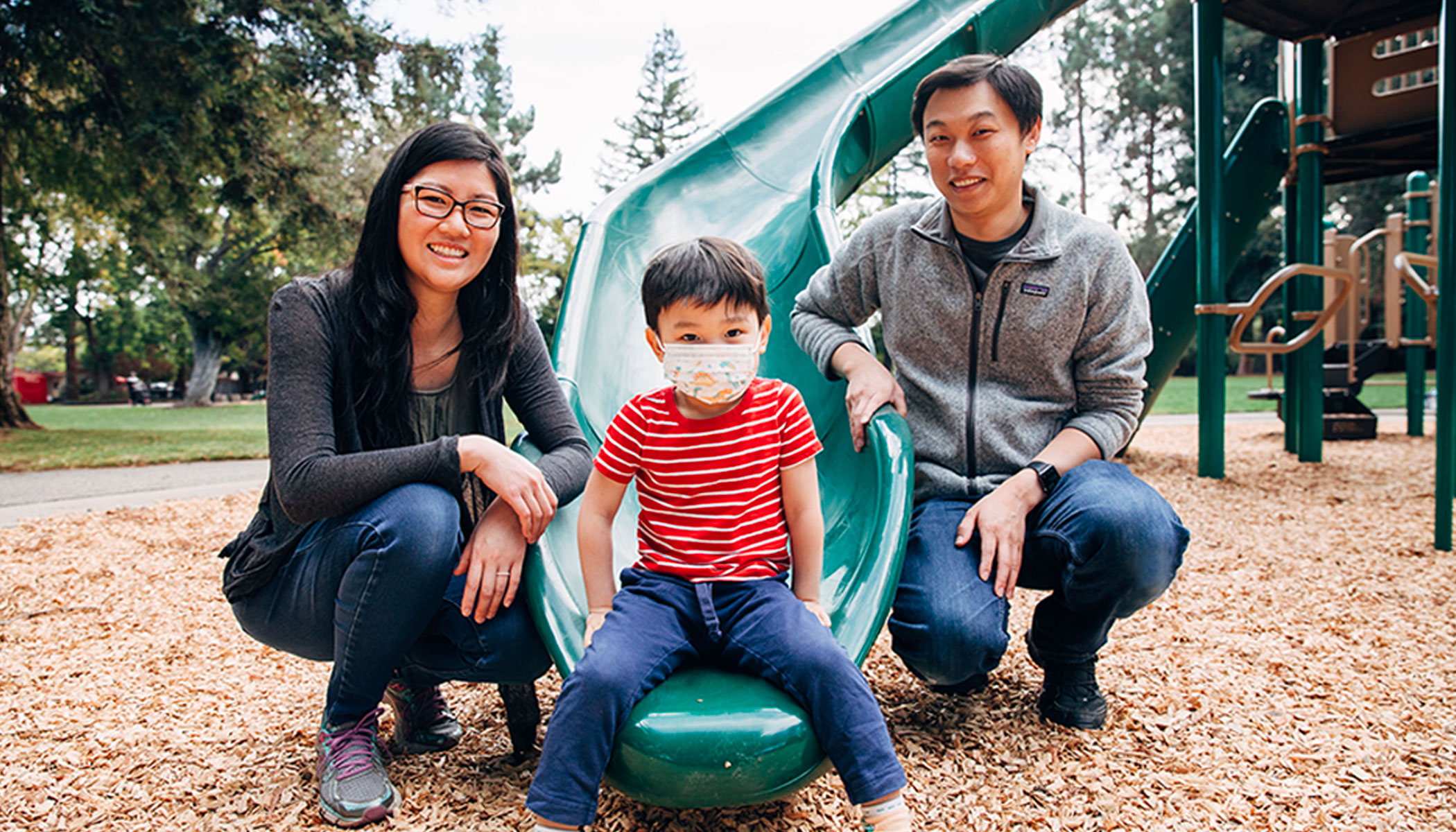A women, child and man pose for a family picture at the foot of a playground slide.