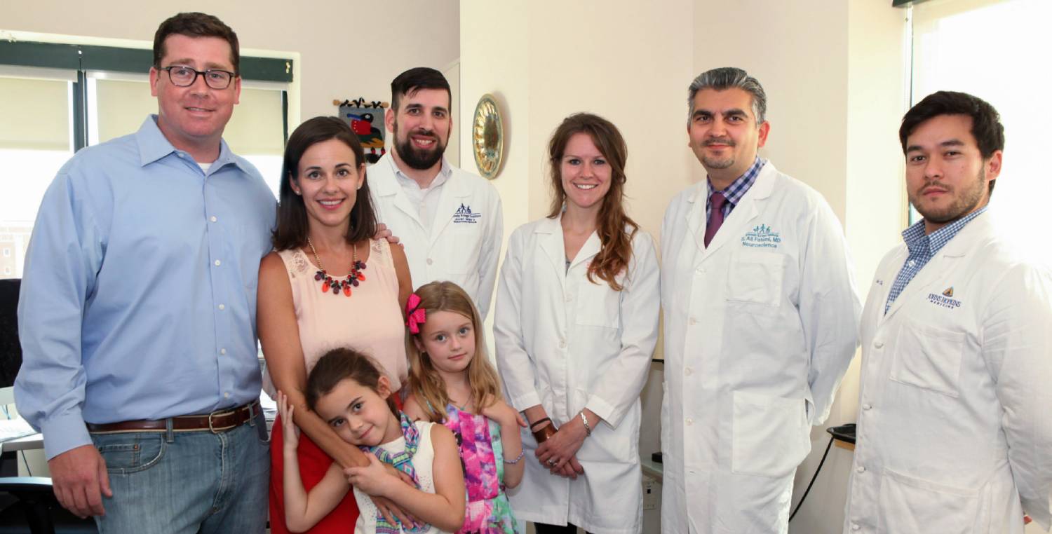 Ellie and her family stand in a clinic with the research team who are all wearing lab coats.