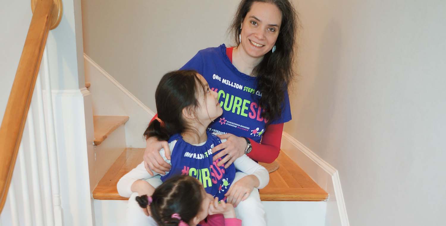 Eszter Hars sits on a wooden staircase, as her two young daughters look back at her, all wearing blue SDS Alliance shirts.