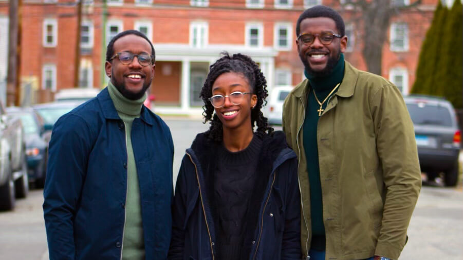 Three adults who all wear glasses, pose and smile together.