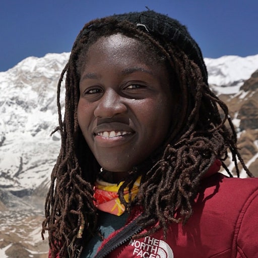 A Black Woman with dreadlocks partially smiling at the camera with a snowy mountain range in the background