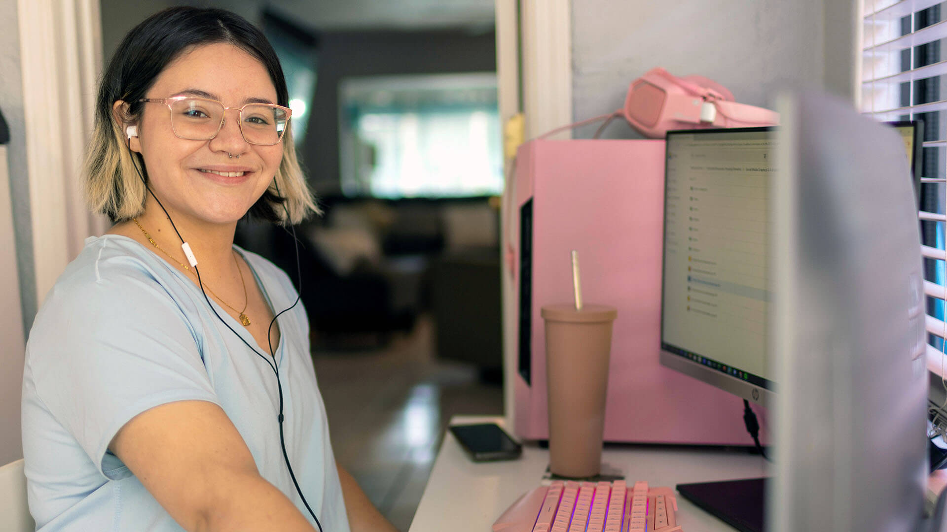 A woman with glasses wears headphones while sitting at a computer.