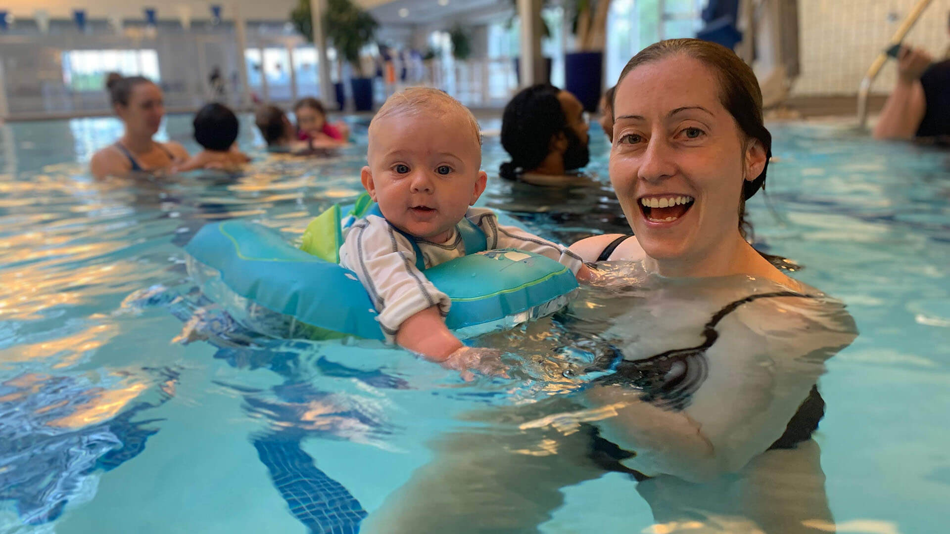 Laura smiles in a swimming pool while holding her 3-year-old son.