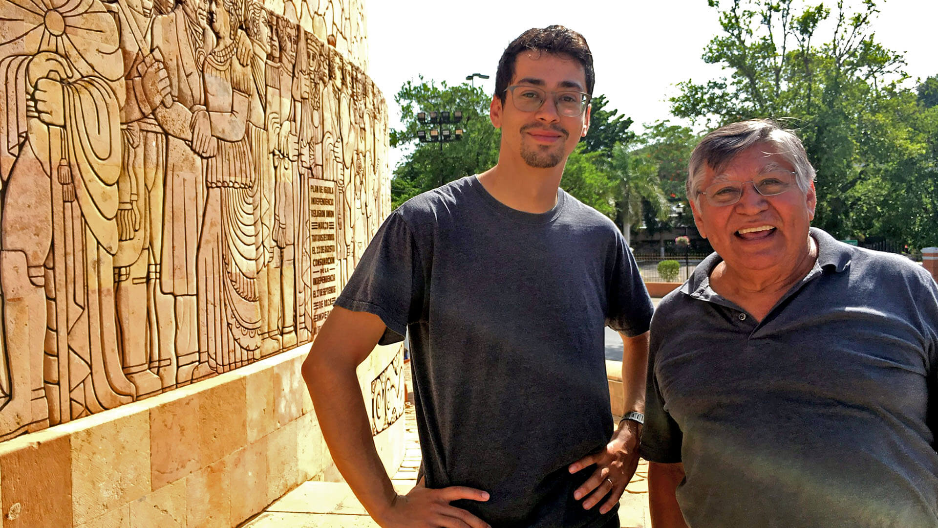 Julio and his dad smile in front of a stone structure with intricate carvings.