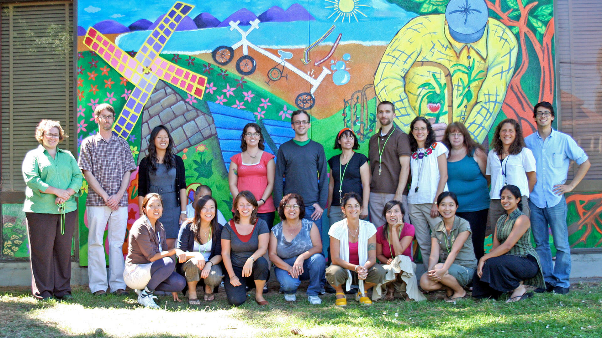  A group of smiling teachers pose for a photo in front of a colorful mural.