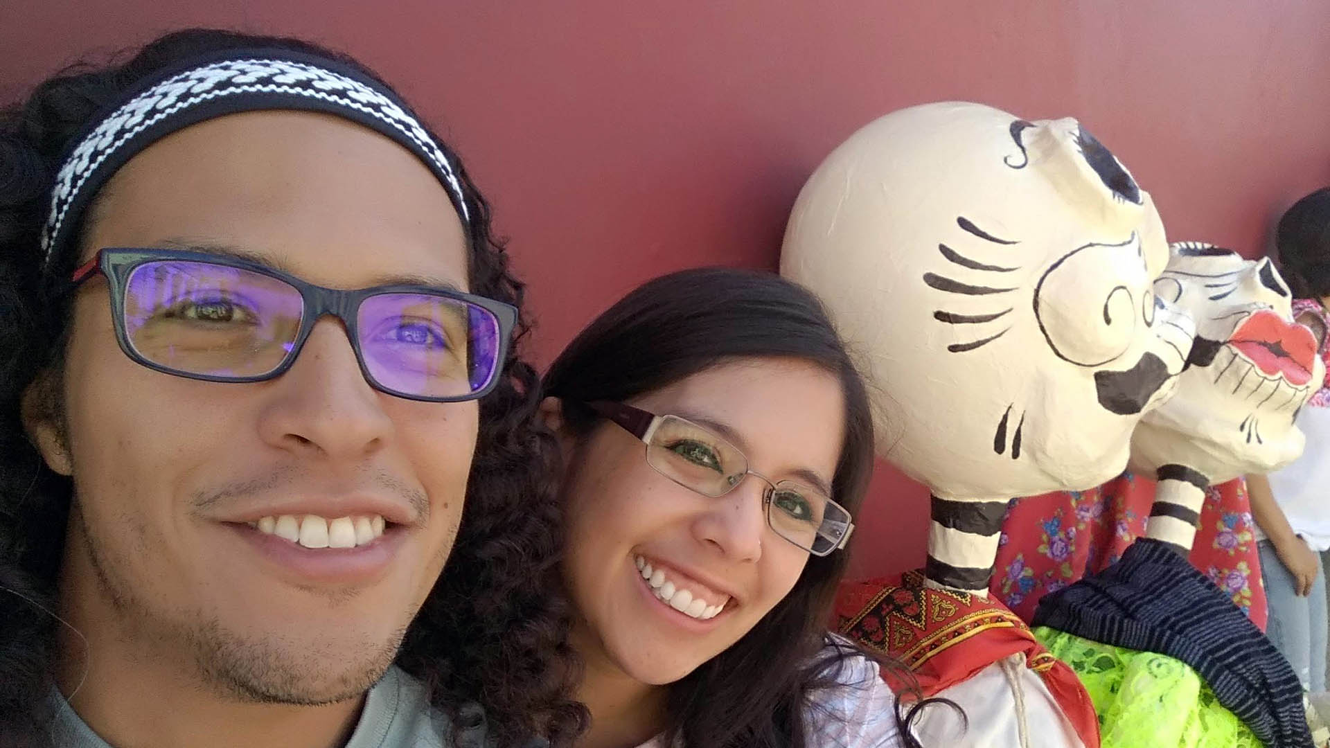 Two people smile for a picture while celebrating Día de Los Muertos. 
