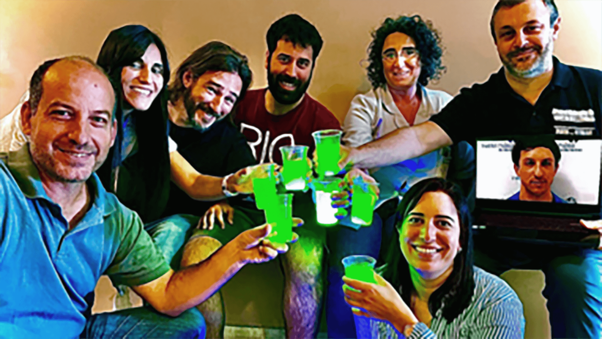 A group of people smile for a photo while toasting with bright green drinks.