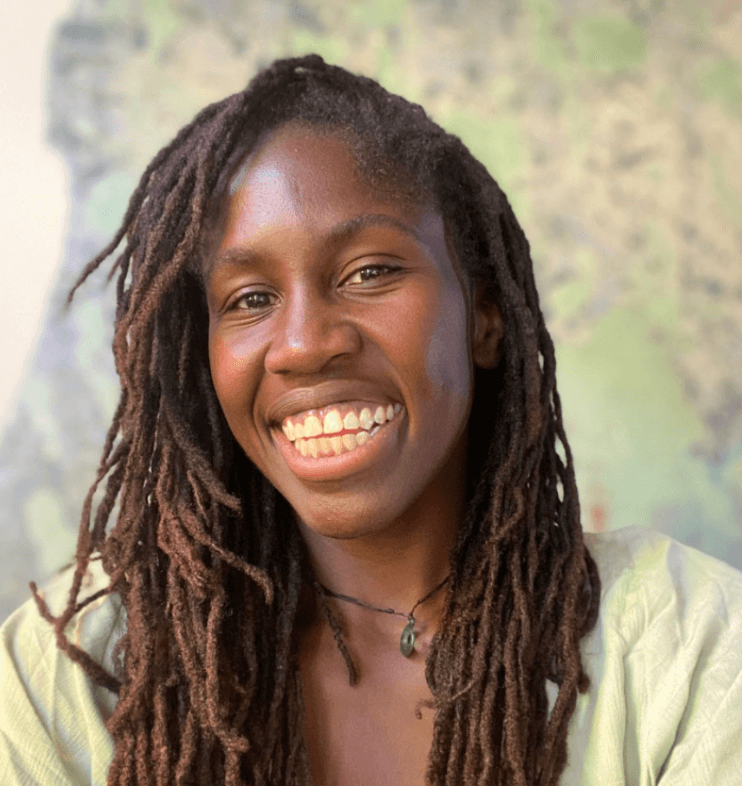 A Black woman with dreadlocks smiling at the camera a green top, and offset background.
