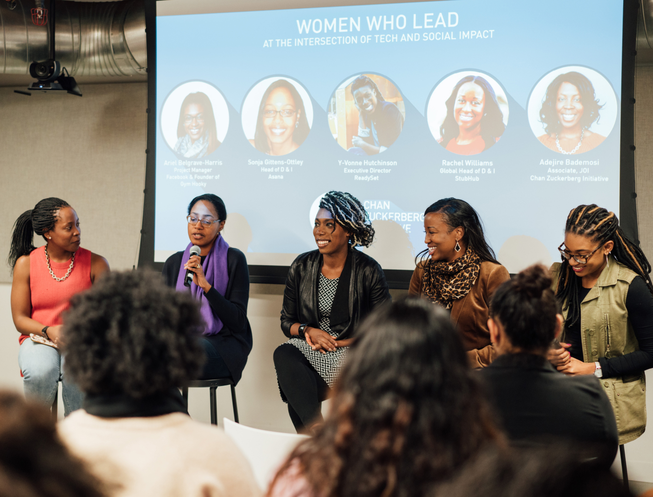 A panel discussion where five women sit on stage, facing a room of attendees