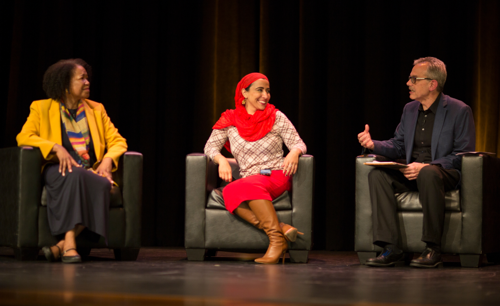 Three people sit in chairs on a stage during a discussion