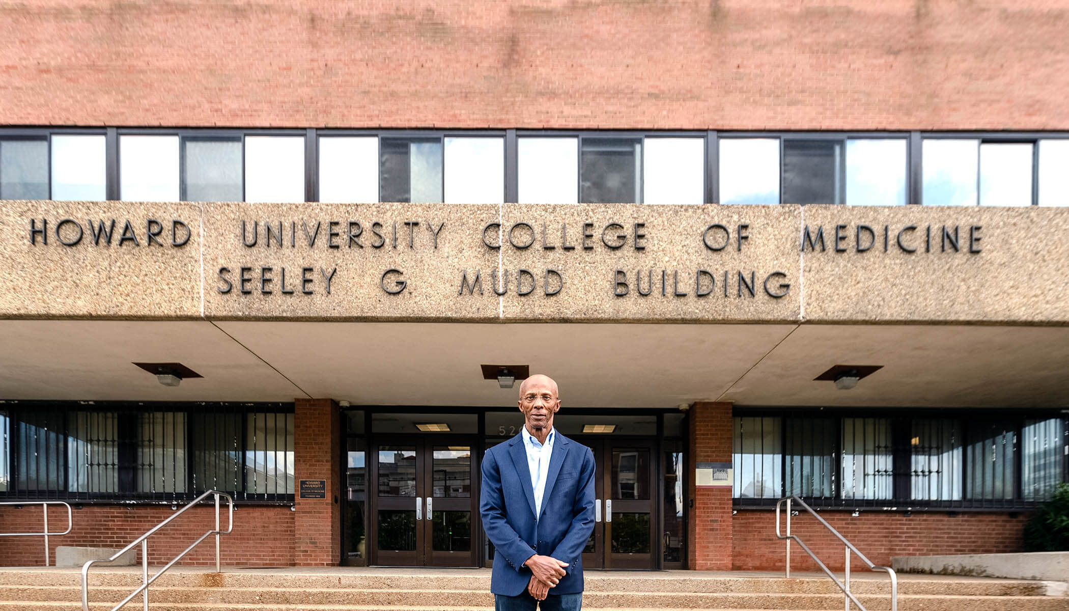 A man stands in front of a campus building that reads “Howard University College of Medicine Seeley G. Mudd Building.”