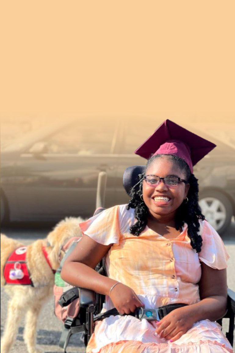 Khari McCrary, a teenage girl, wearing a graduation cap and sitting in a wheelchair, smiles in the school parking lot.
