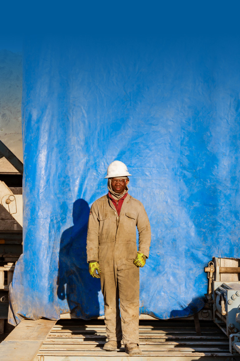 A worker in a hard hat stands in front of a blue surface.