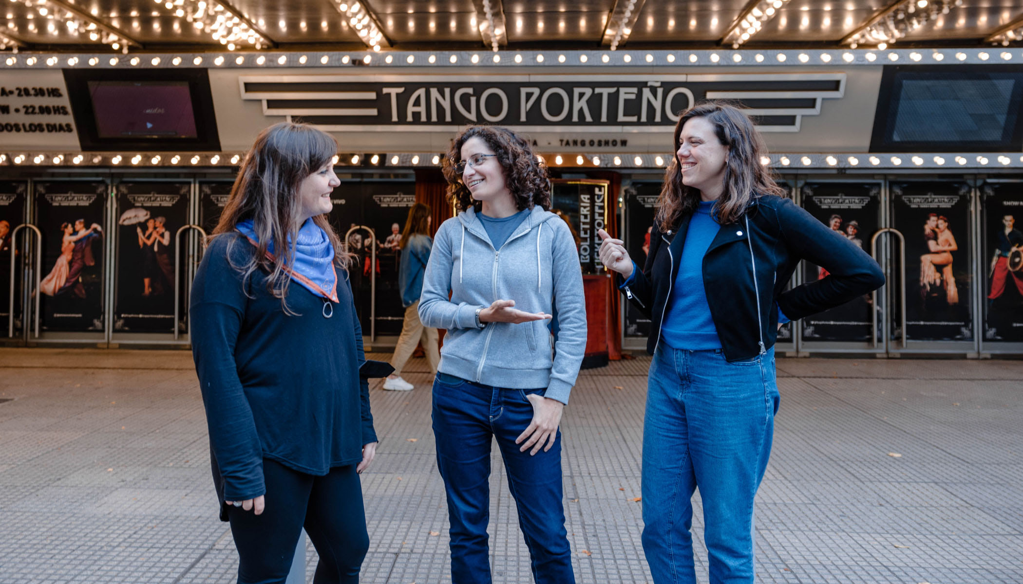 Three people have a conversation in front of a building that says, “Tango Porteño.”