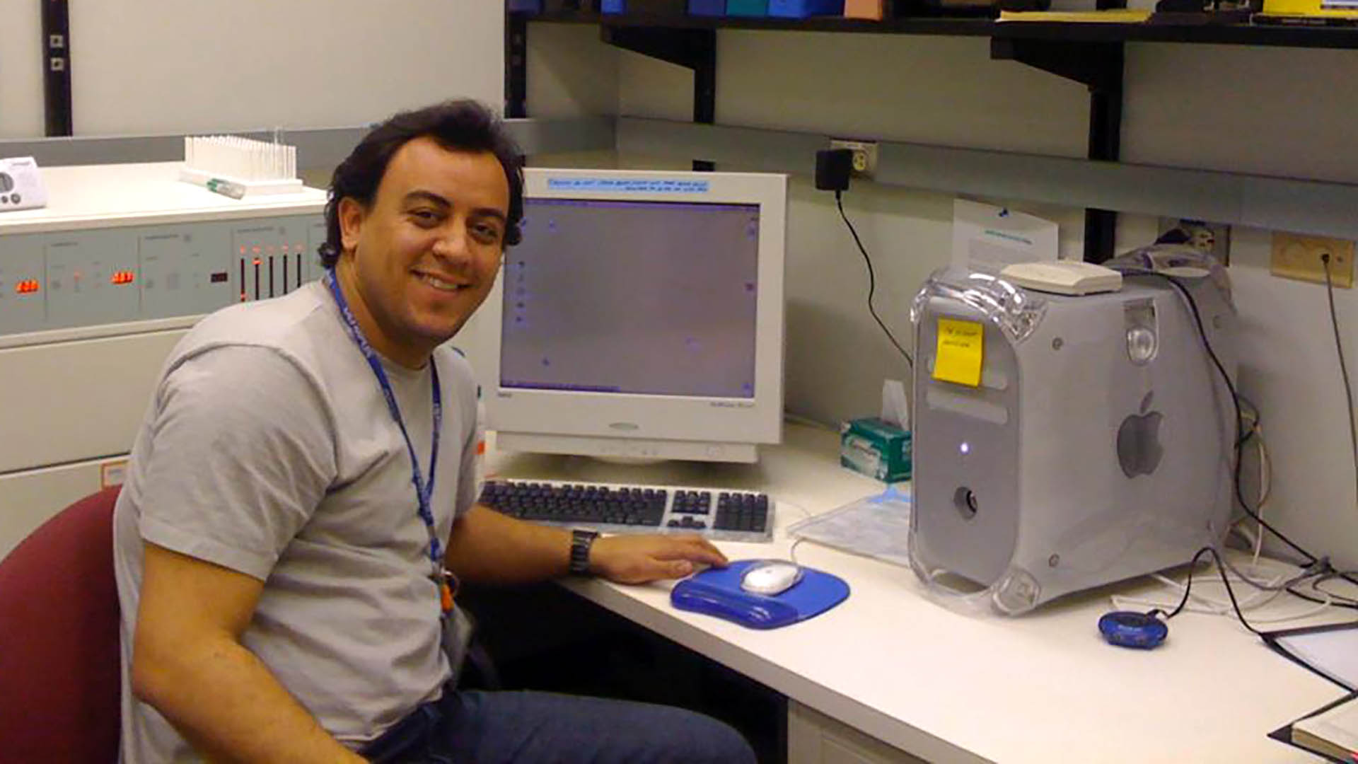 Biologist Gustavo B. Menezes smiles at the camera while sitting at a desk with an older computer.