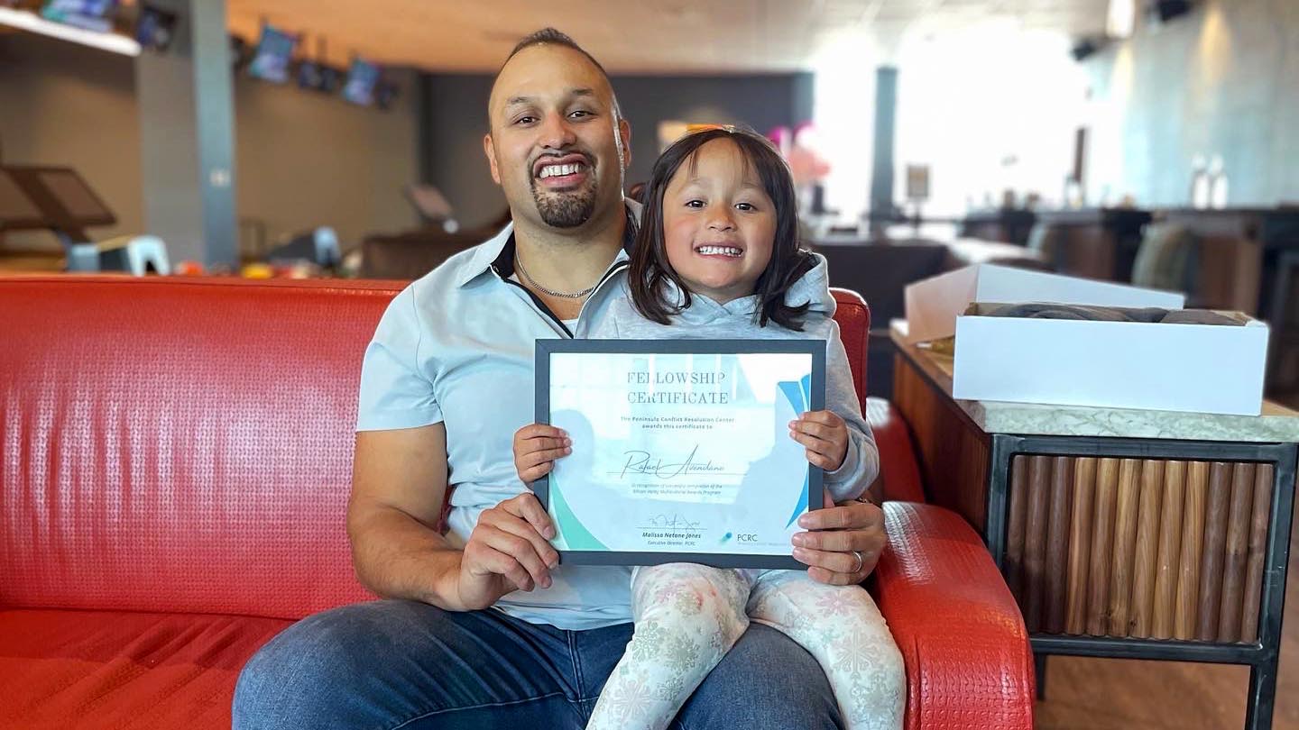 Rafael Avendaño and his daughter hold a fellowship certificate together and smile.