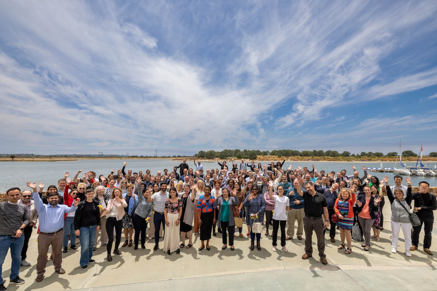 A group of participants at CZI’s Neurodegeneration Challenge Network 2023 Annual Meeting stand side by side in front of a body of water and wave at the camera.