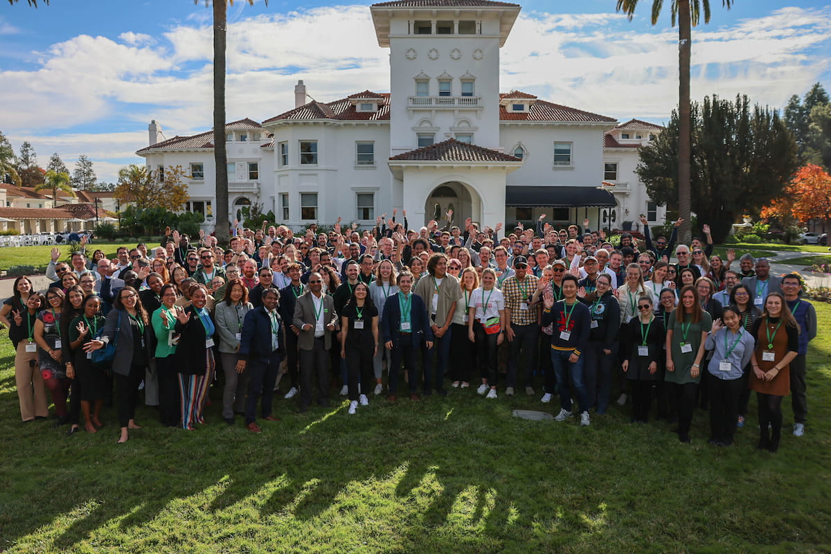 A group of participants at CZI's Single-Cell Biology 2022 Annual Meeting pose waving outside on a lawn in front of a large white building.