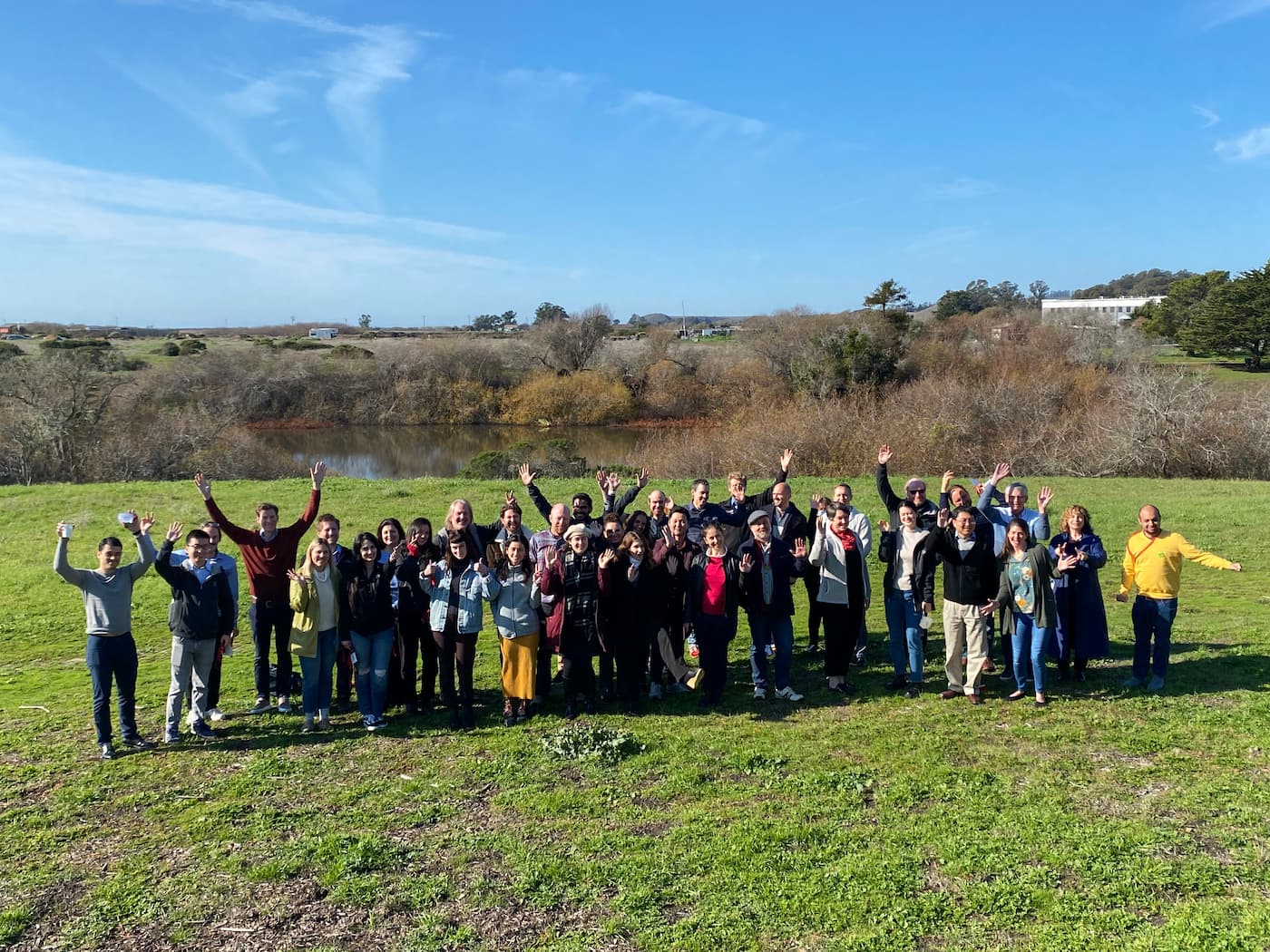 Participants at CZI's Single-Cell Data Ecosystem Workshop stand on a grassy field while waving at the camera