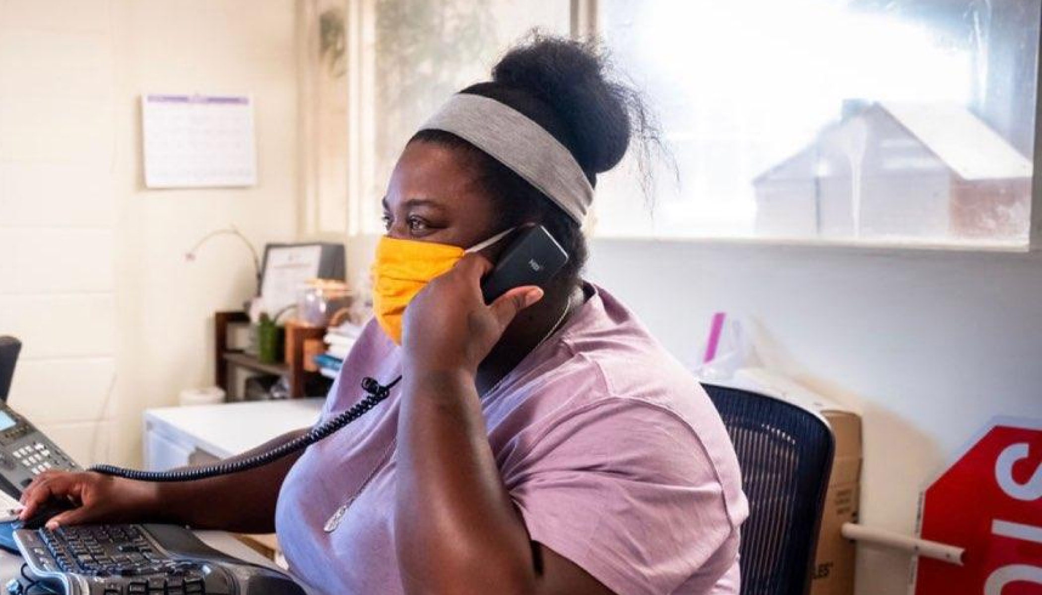 LaKesha Roberts wears a mask while talking on the phone and working at a desk.