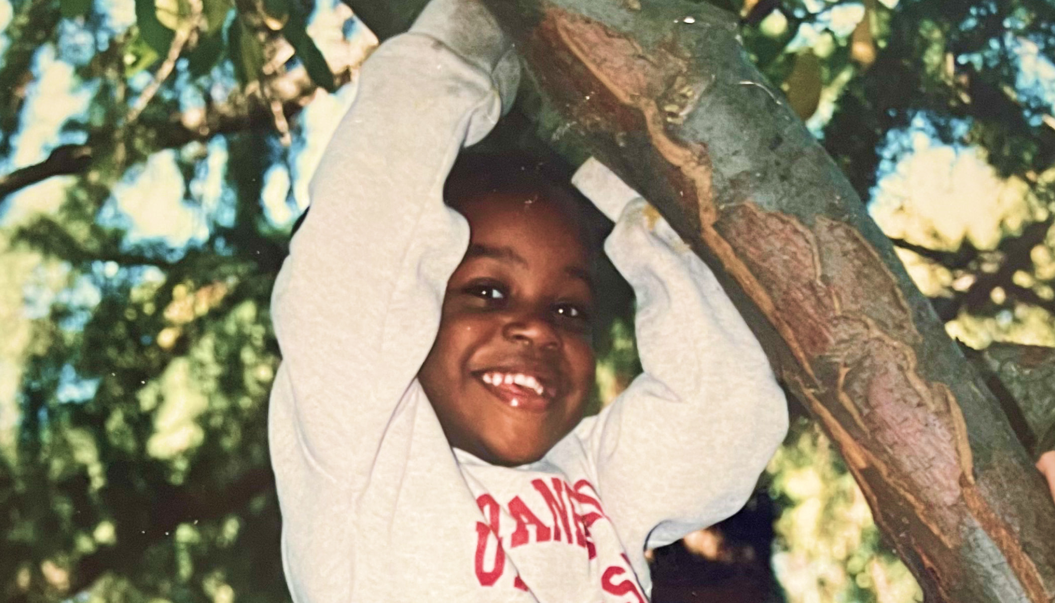 A young LaKesha Roberts holds onto a tree branch and smiles.