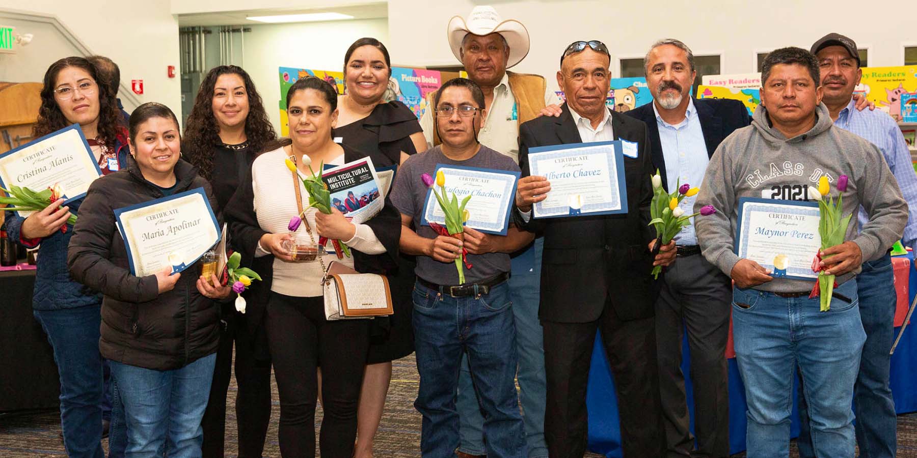 A group of people hold certificates and flowers and pose for a group photo.