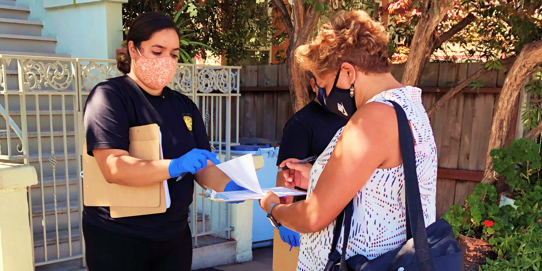 Mirna Cervantes holds a clipboard for a community member while standing outside.