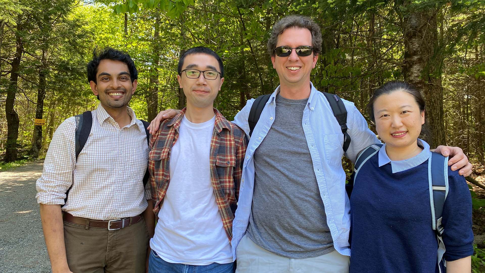 A group of four people, including Nicholas Navin, pose for a photo in a wooded area.