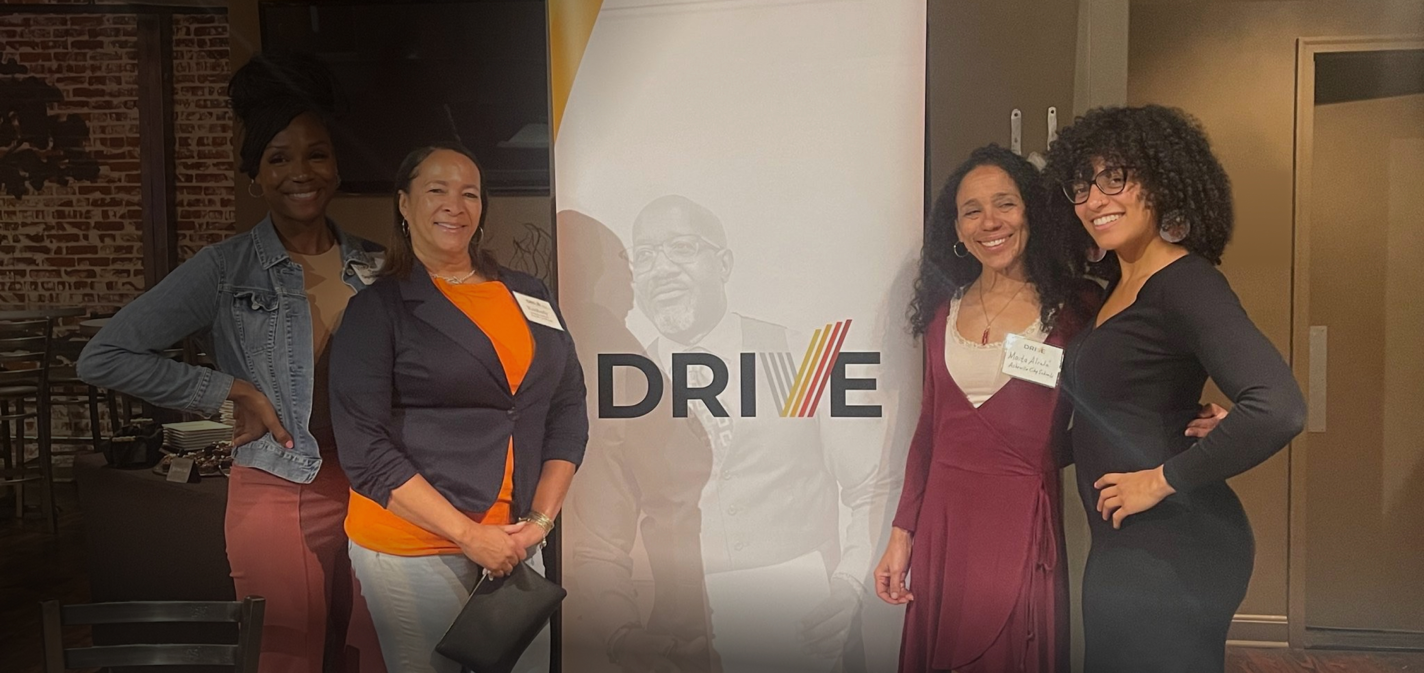 Women posing next to graphic poster with Drive logo.