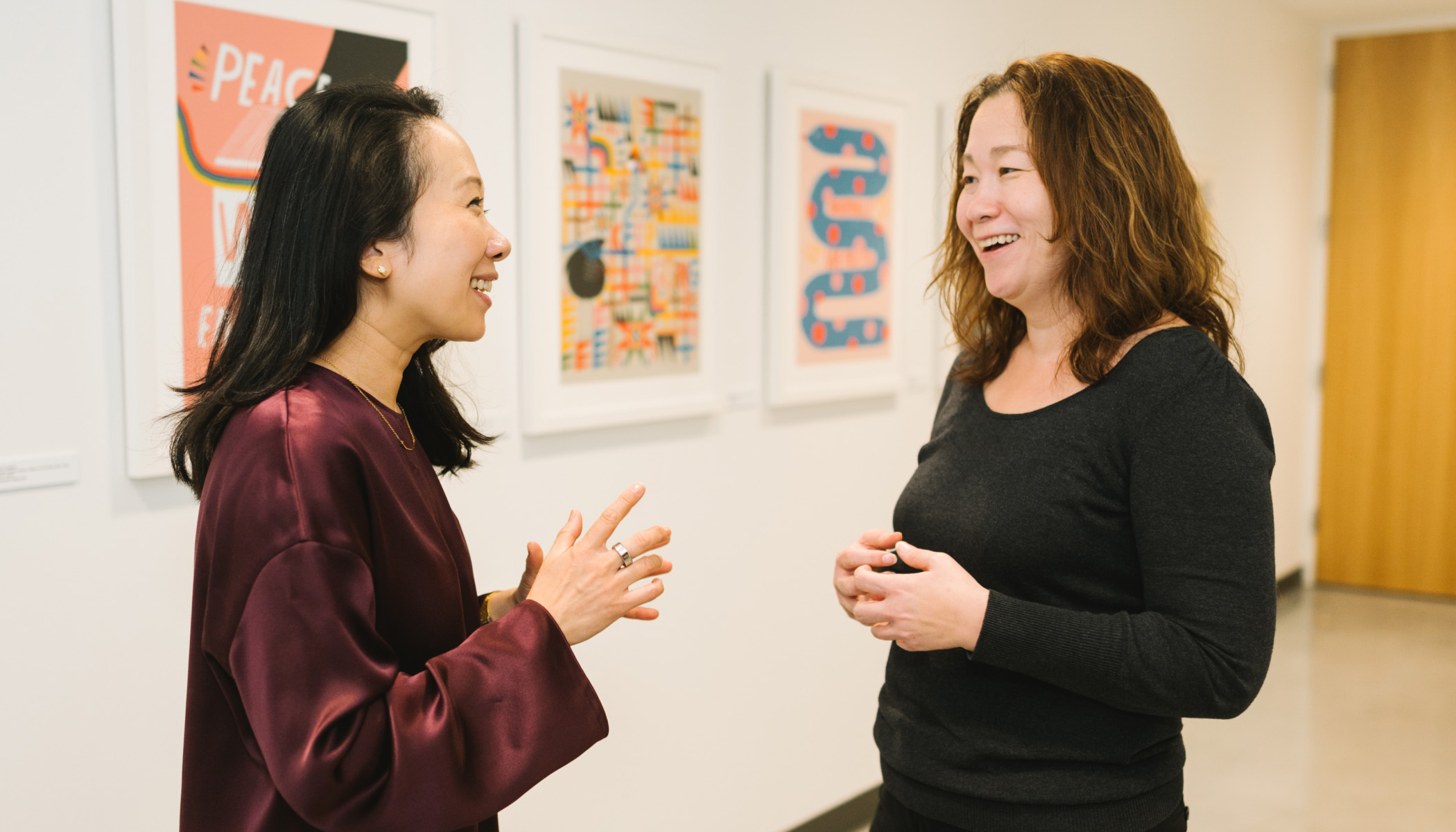 Sandra Liu Huang, CZI’s head of education stands in the hallway at CZI headquarters and faces Monica Milligan, executive director of Gradient Learning. Both are smiling as they speak.