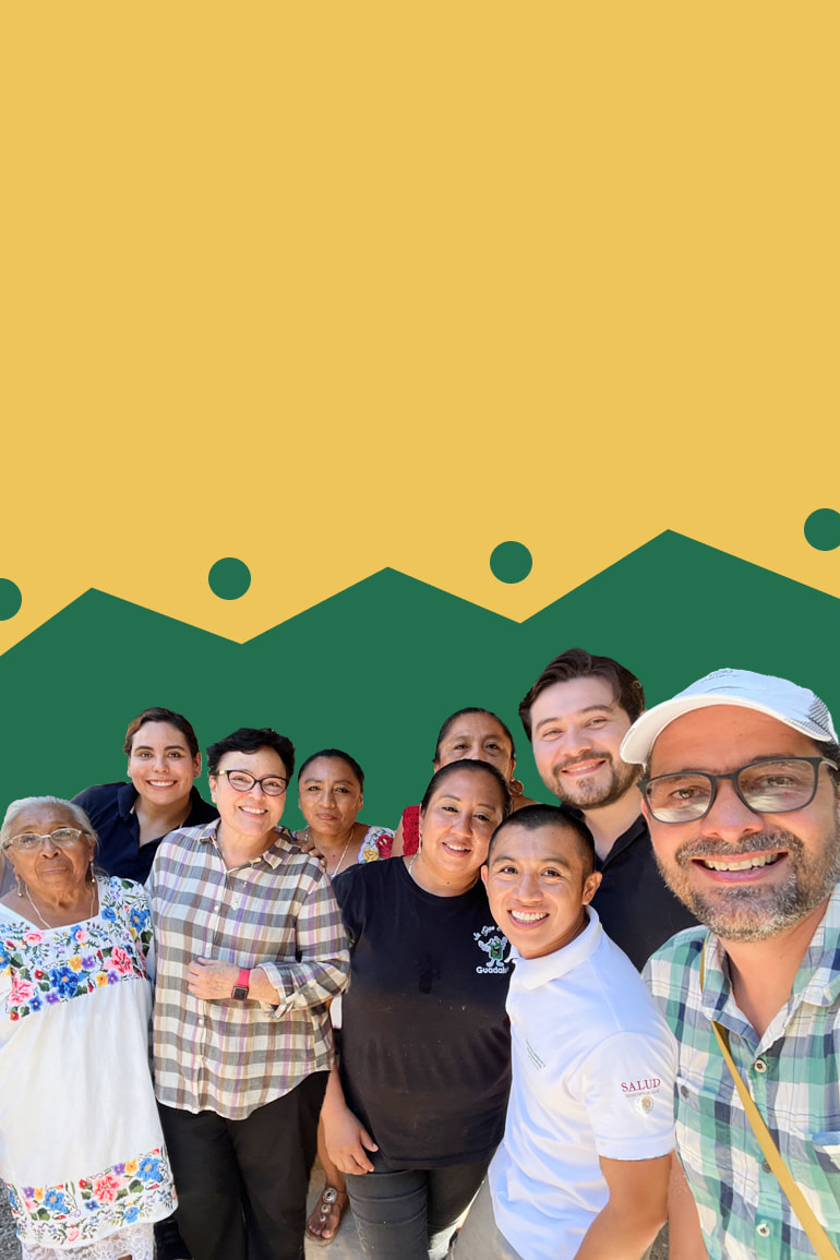 Selfie taken by Andrés, smiling in a cap and glasses in a green and blue checkered shirt with a group of people from the Mayan community smiling next to the research team. Photo on a yellow and green background.