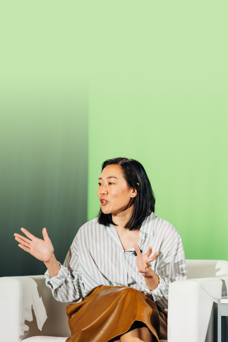 Priscilla Chan talks on a stage with a green background behind her. Her hands are raised as she speaks.