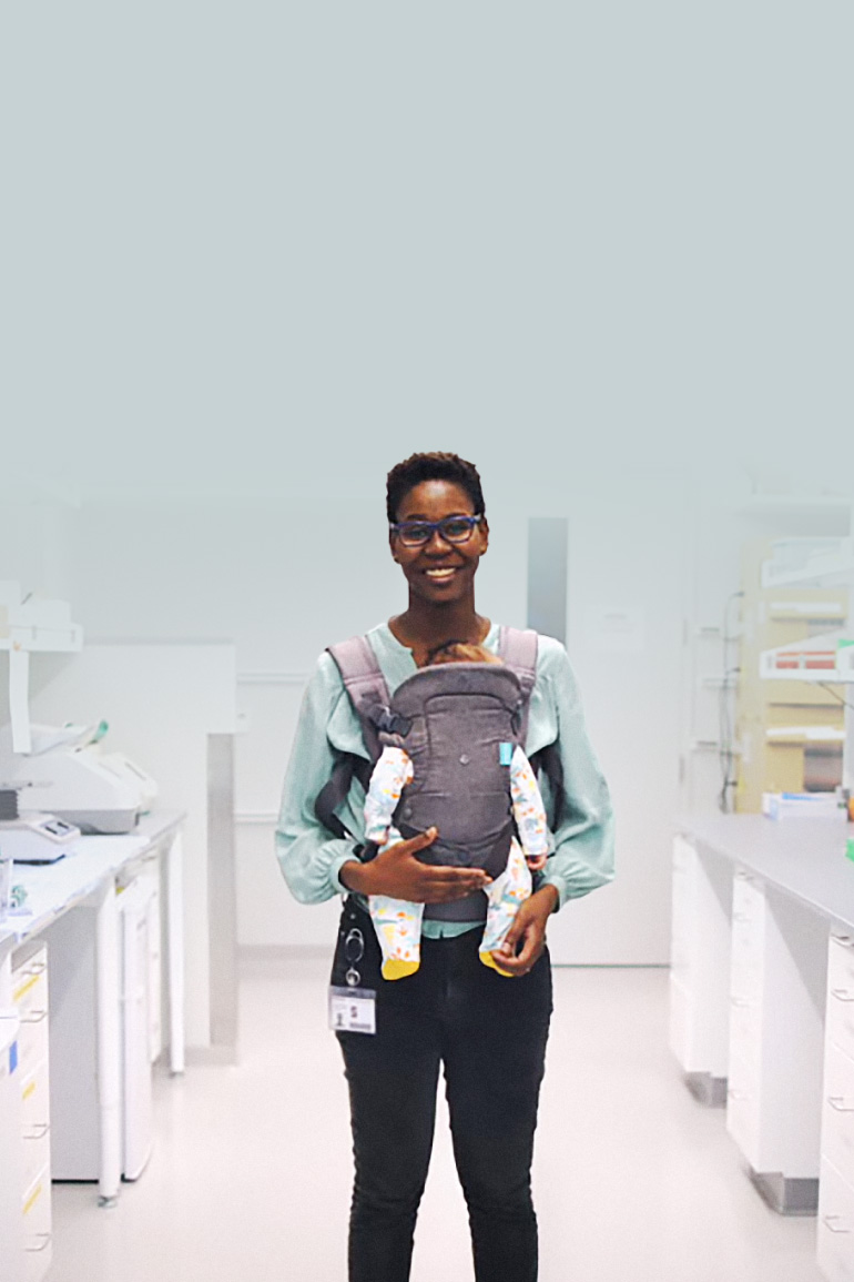 Woman standing holding a baby in a baby carrier in a laboratory setting