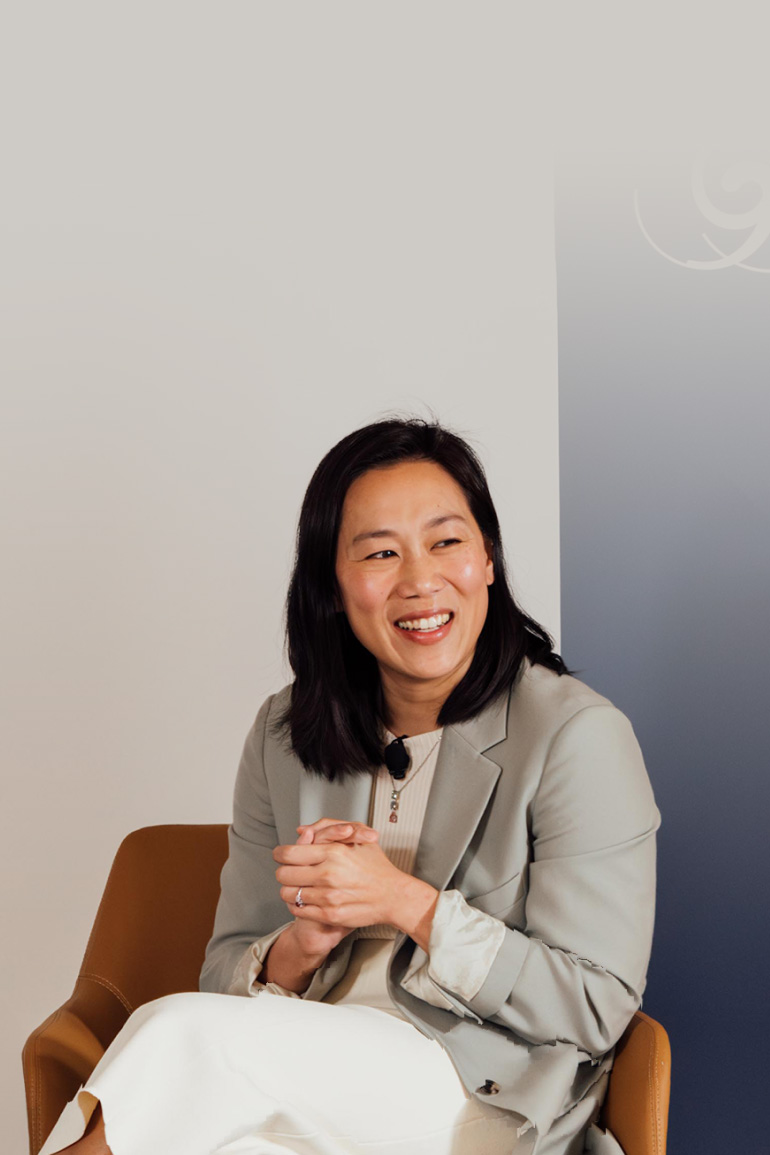 Priscilla Chan sits in an armchair on stage and clasps her hands. She smiles out at the audience.