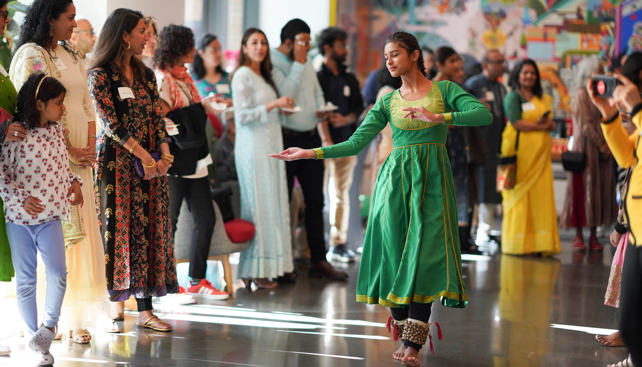 A woman in a green, traditional South Asian dress dances in the middle of a crowd.