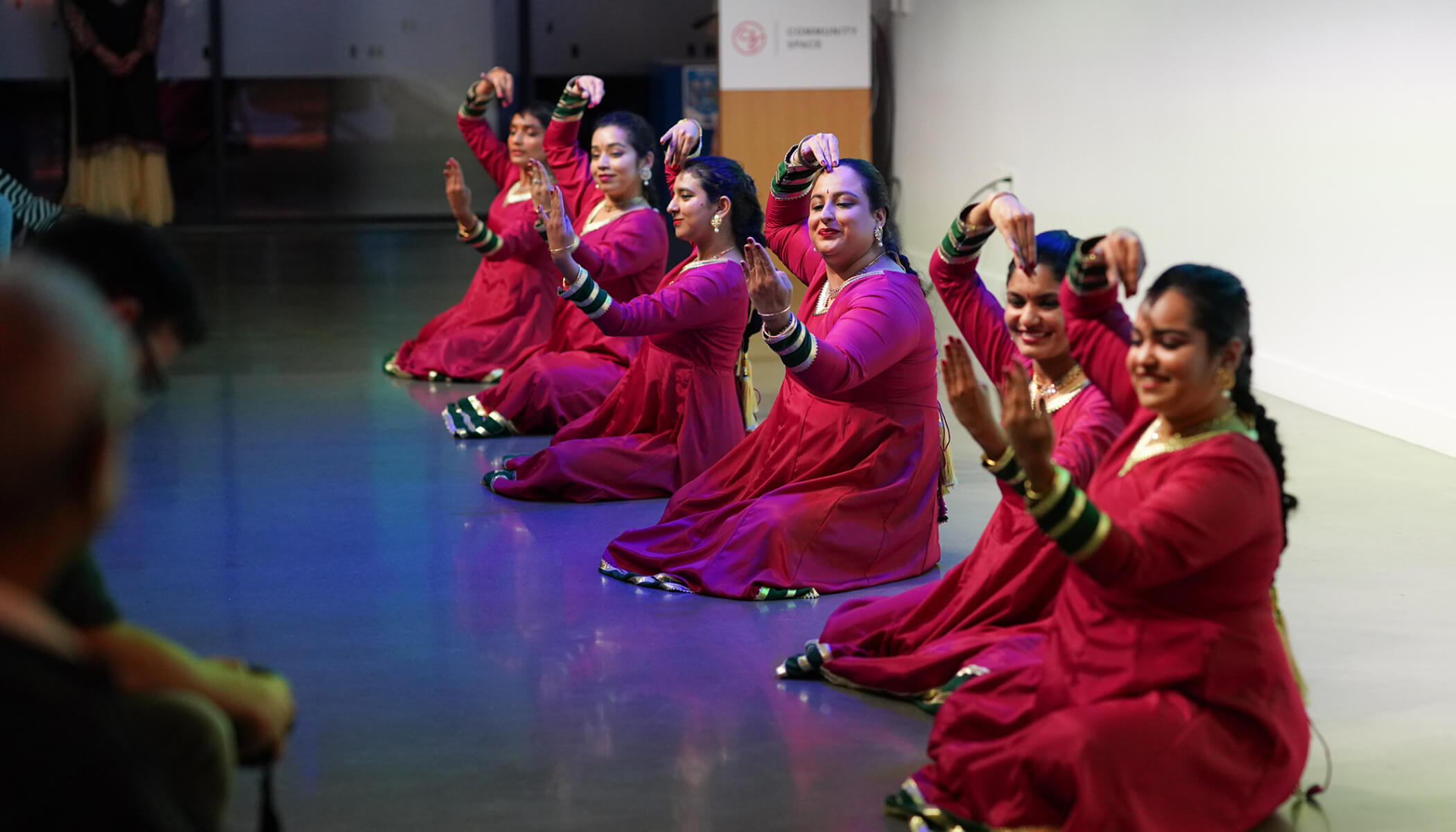 Women in pink sit on the floor during a dance performance.
