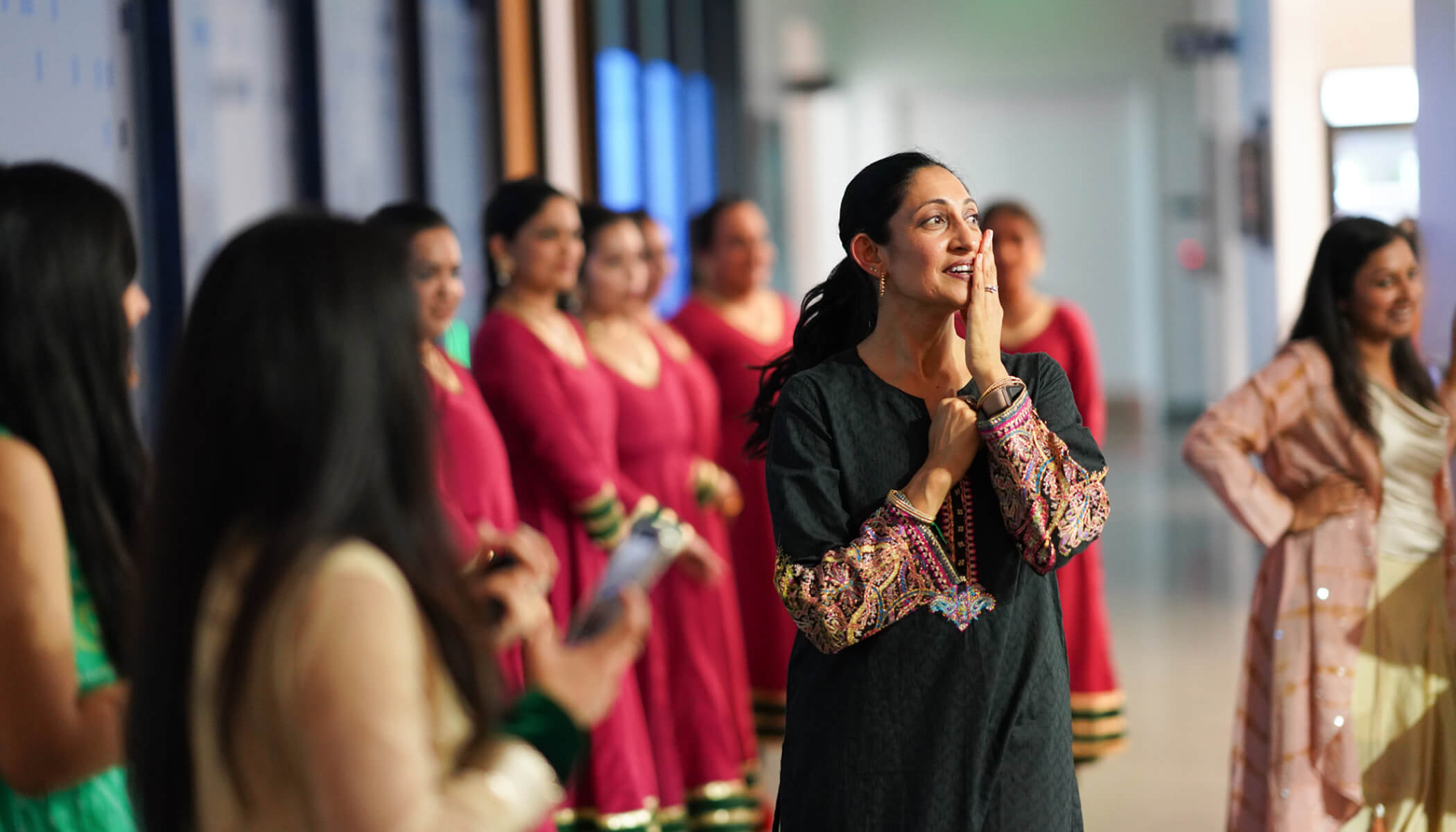 A woman in black South Asian attire touches her cheek during a performing arts event.
