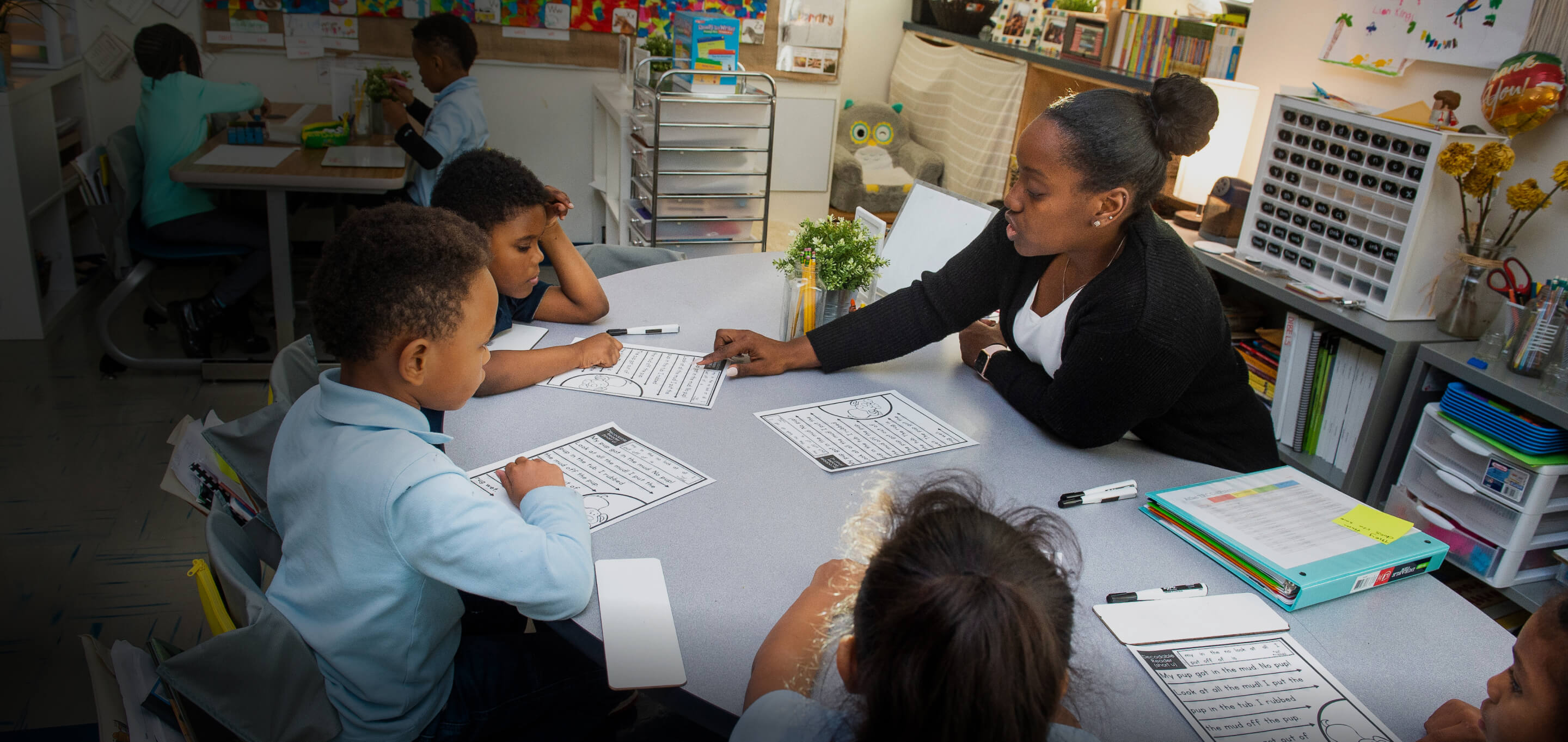 Teacher sitting at a desk and helping students with their work in the classroom