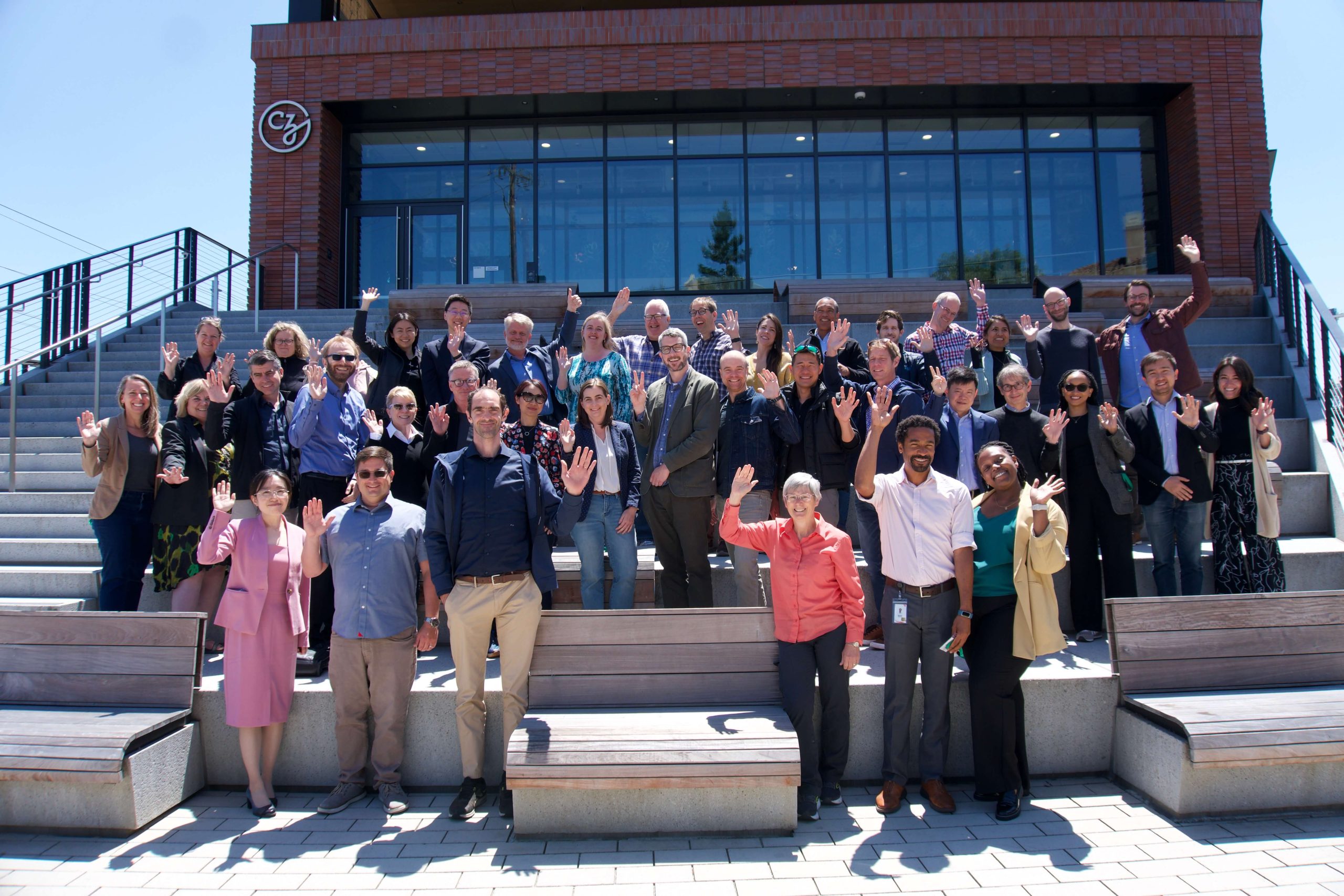 Participants of the Exploratory Cell Networks Kickoff Meeting waving on the steps at the CZI headquarters in Redwood City, CA.