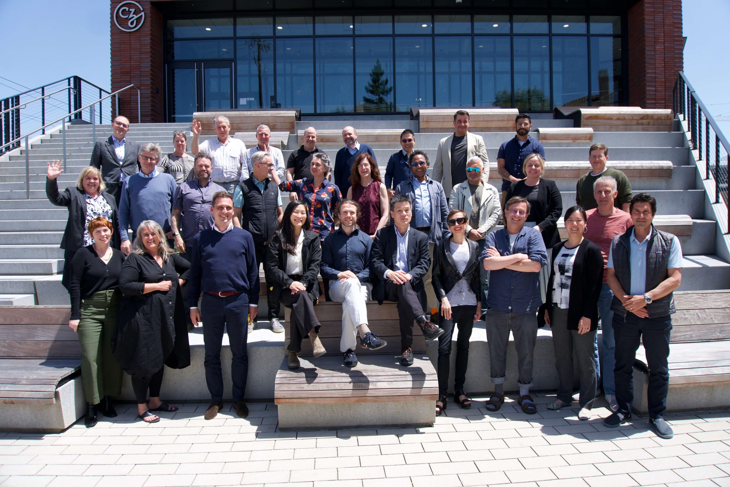 Participants of the CZI Fundamental Neuroscience Workshop: Plasticity Across Scales wave at the camera on the steps at the CZI headquarters in Redwood City, CA.