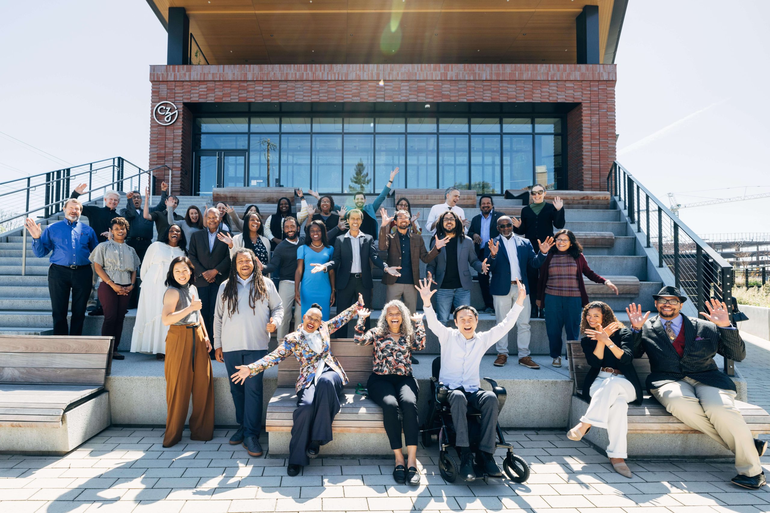 Participants of the Science Diversity Leadership stand outside waving to the camera with the CZI building in the background.