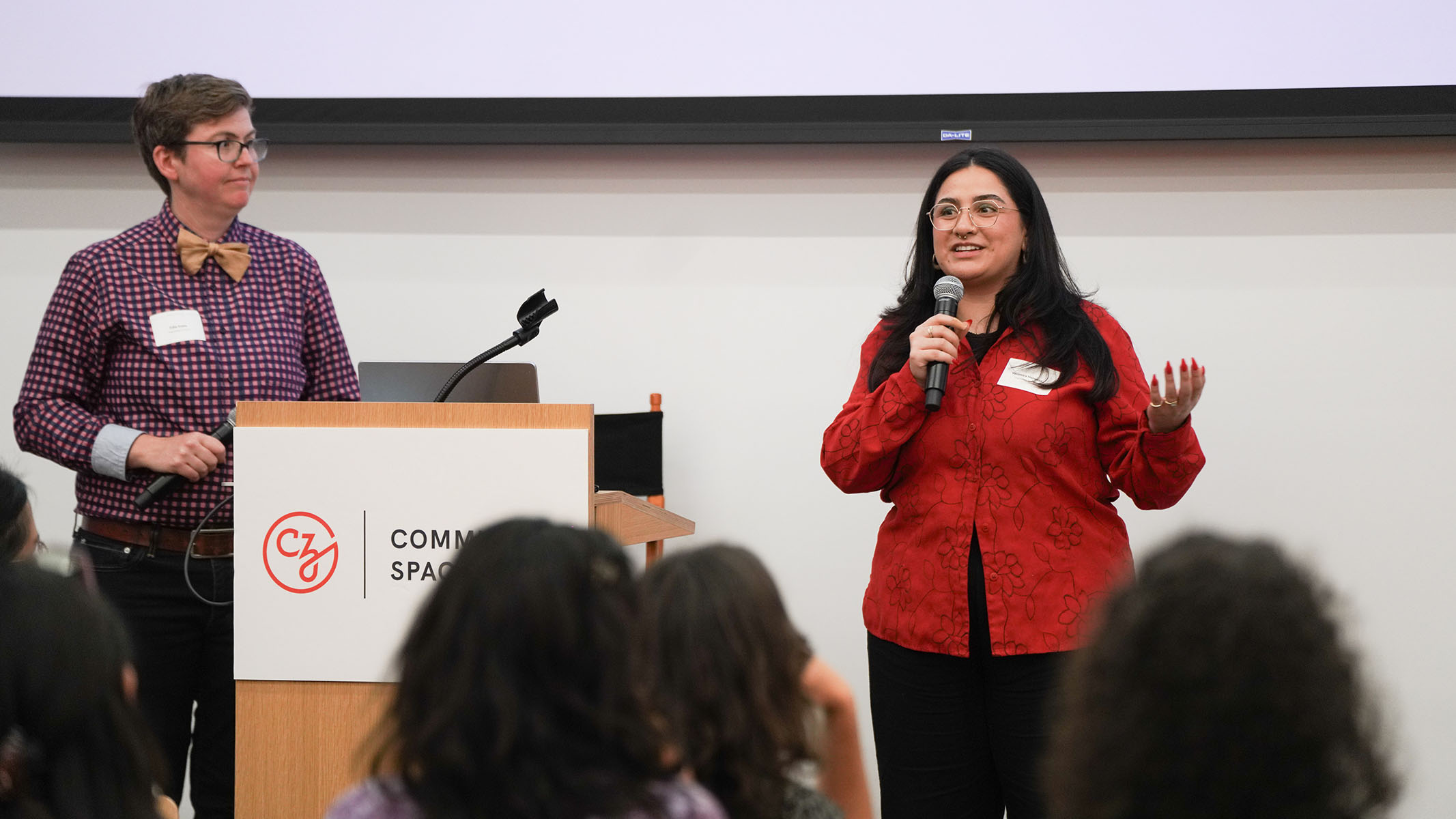 Two people hold microphones beside a podium.