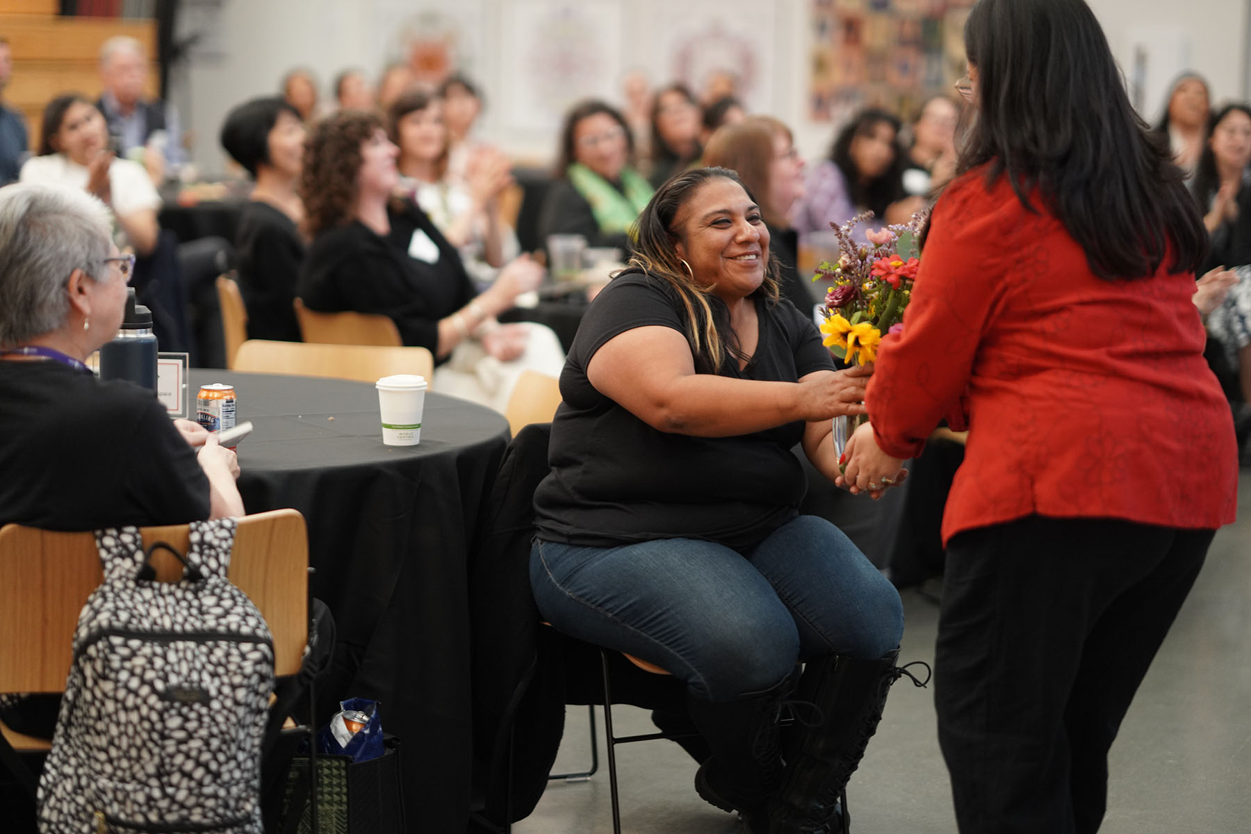 A woman who is seated receives flowers from a woman in a red shirt.