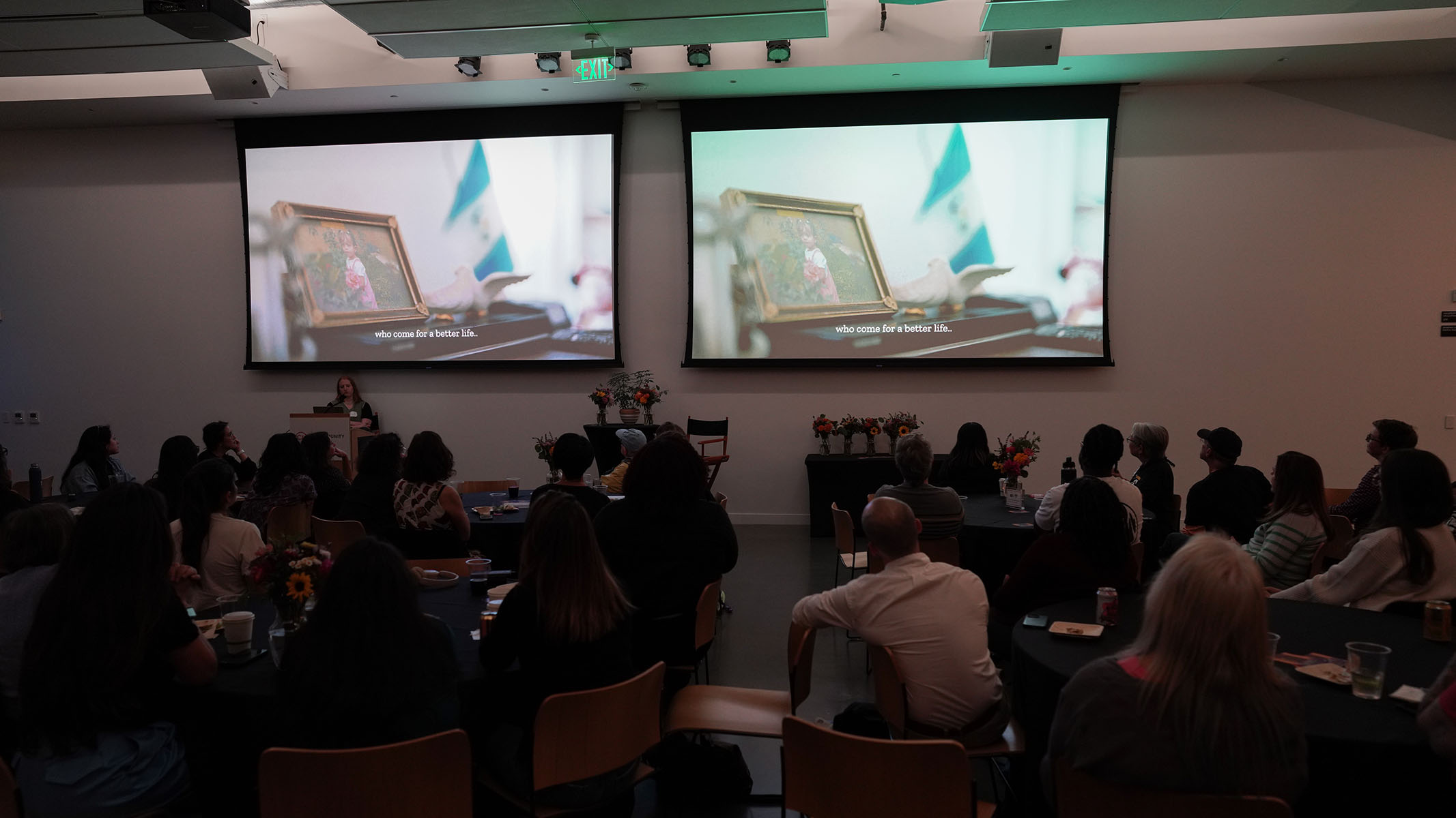 A few dozen people sit in a dark event space as two large projectors play short films.