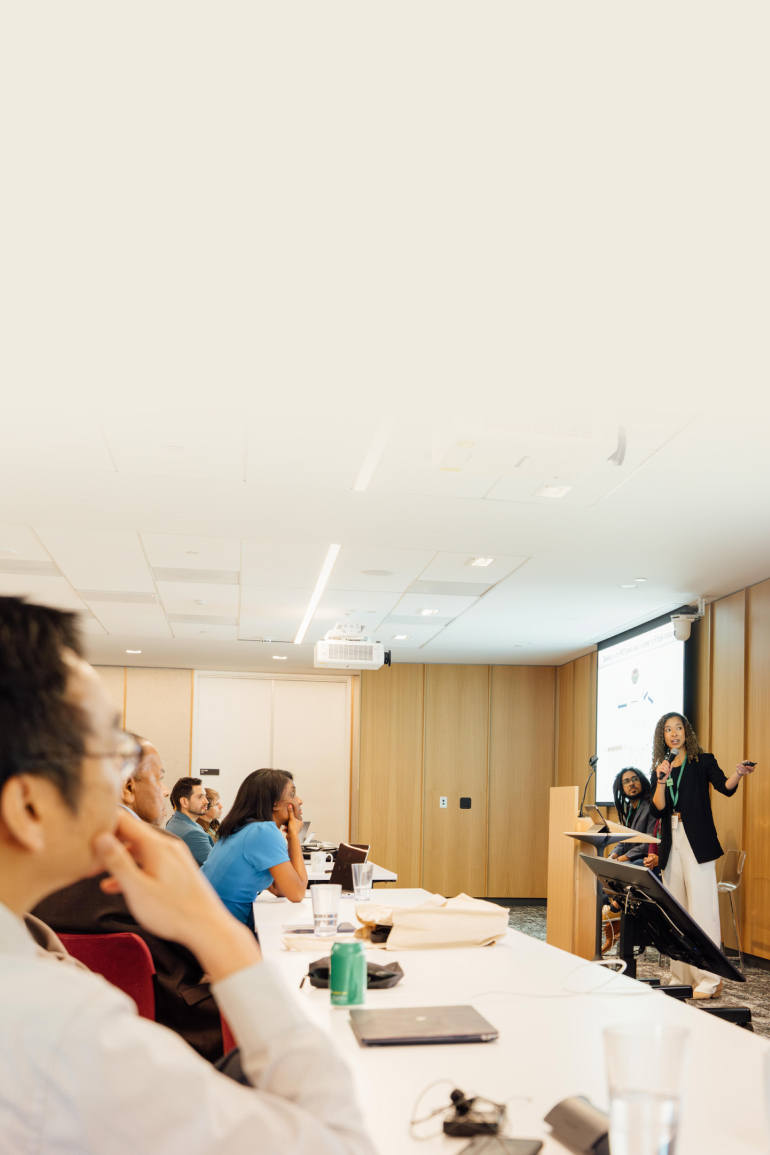 A woman stands at the front, delivering a presentation to a group of attentive listeners.