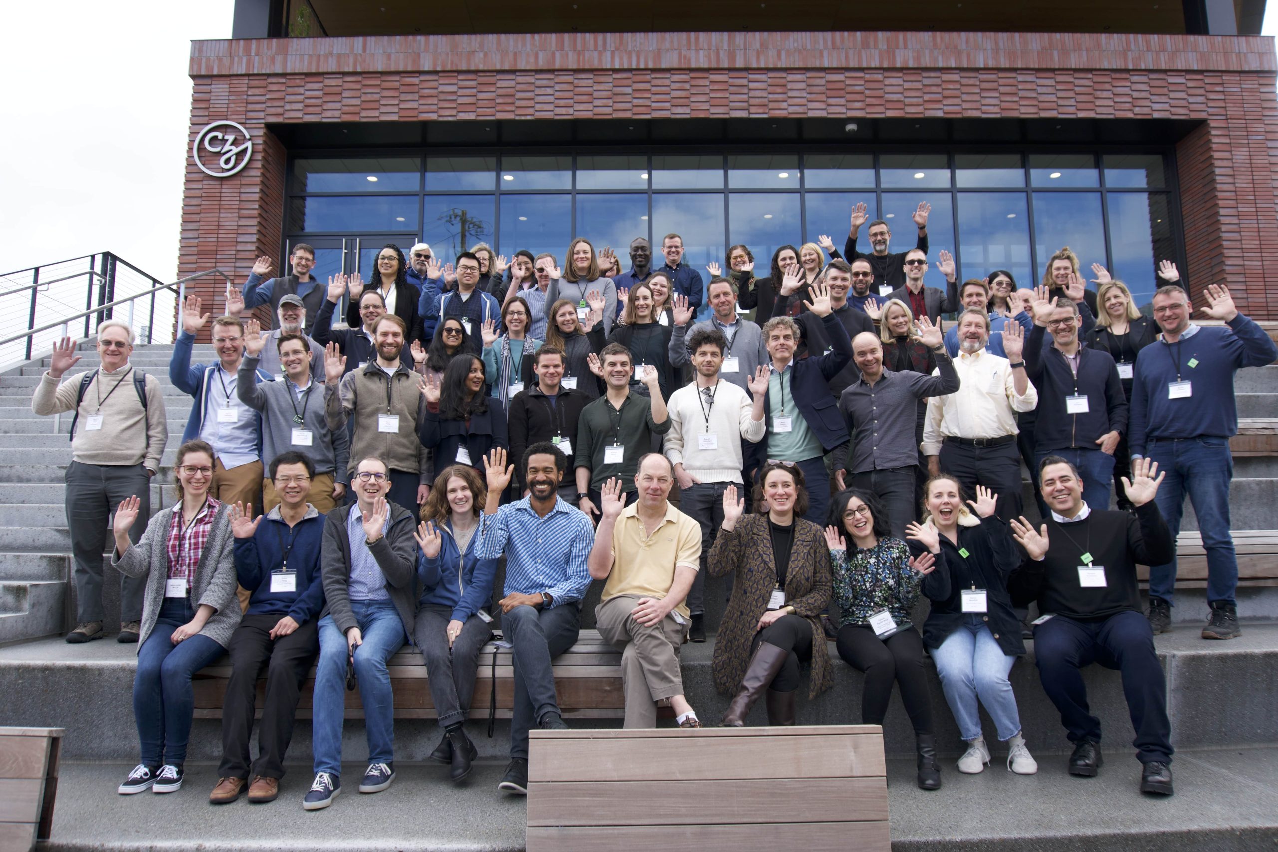 Participants of the Metabolism Network Kickoff Meeting stand on the steps outside of CZI’s headquarters. They smile and wave at the camera.